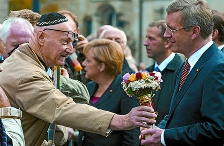 Un hombre con la 'kipá' judía ofrece flores a Wulff, ayer en Bremen, en presencia de la cancillera Angela Merkel.