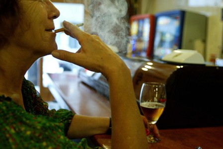 Una mujer fuma mientras toma una consumición en la barra de un bar.