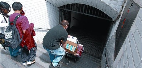 Un hombre cargado con cajas desciende penosamente por las escaleras del metro de Arc de Triomf.